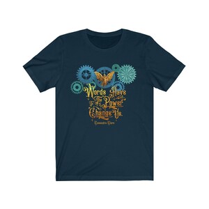 Puede incluir: Una camiseta azul marino con un dise&ntilde;o gr&aacute;fico de una criatura alada dorada con engranajes y el texto "Words Have The Power To Change Us. Cassandra Clare"