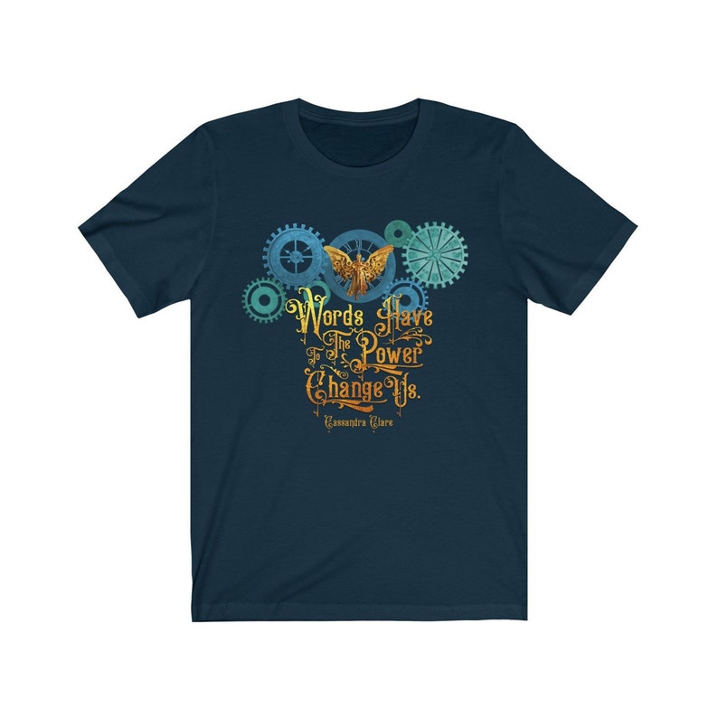 Puede incluir: Una camiseta azul marino con un dise&ntilde;o gr&aacute;fico de una criatura alada dorada con engranajes y el texto "Words Have The Power To Change Us. Cassandra Clare"