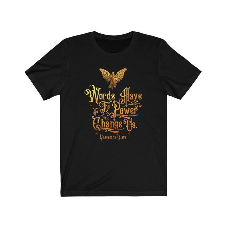 Puede incluir: Camiseta negra con un gr&aacute;fico dorado de un &aacute;ngel y la cita "Las palabras tienen el poder de cambiarnos." de Cassandra Clare.