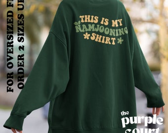 May include: Green oversized sweatshirt with the text "This is my Namjooning Shirt" in a retro font with flower accents. The text is on the back of the sweatshirt. The sweatshirt is from the Purple Court.