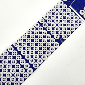 May include: A blue bookmark adorned with rows of white buttons. The buttons are evenly spaced across the bookmark's surface. The bookmark has a rectangular shape with a slightly irregular top edge.