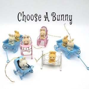 May include: A set of ten miniature bunny ornaments, each in a different pastel-colored vehicle. The vehicles include a stroller, a rocking chair, a wagon, a crib, and a high chair. The text "Choose A Bunny" is printed above the ornaments.