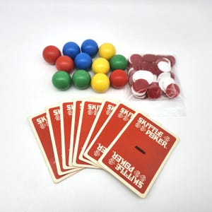May include: A Skittle Poker game set featuring a fan of red playing cards with white text, a collection of small spherical game pieces in red, blue, yellow, and green, and a clear plastic bag containing red and white circular game tokens.