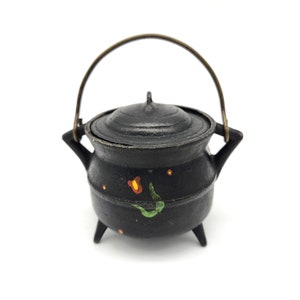 May include: A small black cast iron pot with a lid and a brass handle. The pot has a floral design painted on it in green, orange, and yellow.