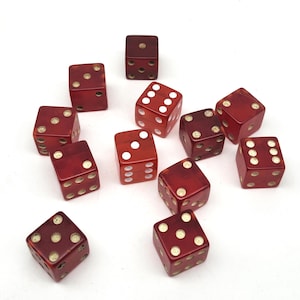 May include: A collection of twelve red dice with white dots, scattered on a white surface. The dice show various numbers from one to six. The dice are a deep red color, and the dots are a creamy white.