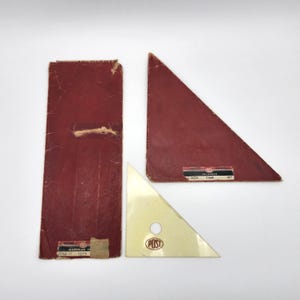May include: Two red cardboard packages for drafting triangles, one labeled "Triangle 7144B 45°" and the other "Style 11 7144A". A clear plastic 45-degree triangle with a "POST" logo is in the foreground.