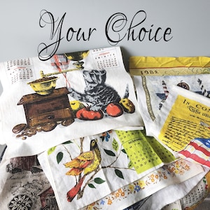 May include: A collection of vintage kitchen towels with various designs. One towel features a cat with a coffee grinder and calendar, another has a bird on a branch, and others display patriotic themes and text. The words "Your Choice" are written in cursive.