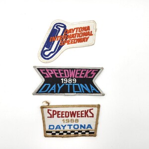 May include: Three vintage Daytona International Speedway patches. The top patch features a racetrack design with "Daytona International Speedway" text. The middle patch reads "Speedweeks 1989 Daytona". The bottom patch reads "Speedweeks 1988 Daytona".