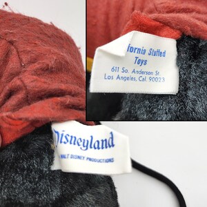 May include: Close-up of a vintage plush toy with a red head and black body. The toy has two tags, one reading "fornia Stuffed Toys" and the other "Disneyland Walt Disney Productions". The tags provide the address of the manufacturer.