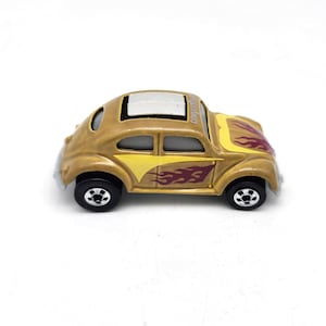 May include: A gold-colored toy car with black wheels and a sunroof. The car features yellow and maroon flame decals on the sides and hood. The text "CONVERTIBLE" is printed on the roof.
