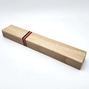 May include: A wooden box with a red, black, and white stripe design. The box is made of light wood and has a smooth finish.