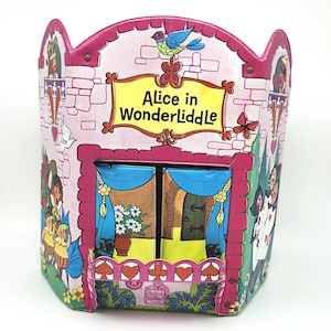 May include: A pink metal container featuring the text Alice in WonderLiddle, decorated with illustrations of a castle, a blue bird, playing card characters, and a balcony with blue curtains, flowers, and red card suit symbols on the front.
