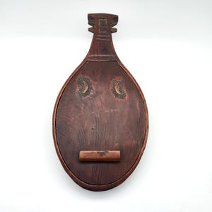 May include: A dark brown wooden box shaped like a lute with a carved design and two brass crescent moon inlays. The box has a hinged lid and a wooden latch.
