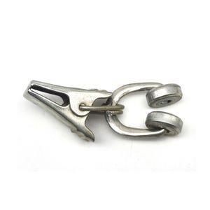 May include: A silver-colored metal clip with a spring-loaded clamp on one end and two rounded magnetic attachments on the other. The clip is designed to hold items together. The object is on a white background.
