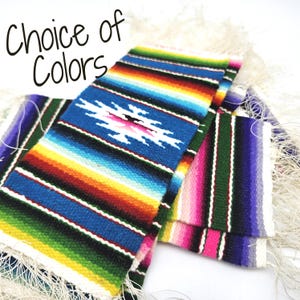 May include: A collection of woven fabric runners featuring vibrant horizontal stripes in blue, green, yellow, orange, pink, and purple with white fringe edges. The text Choice of Colors is printed in black in the upper left corner of the image.