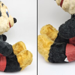 May include: Vintage Mickey Mouse plush toy. The plush features a black body, red shorts, yellow feet, and a cream-colored face. The toy has a black tail and is in a seated position.