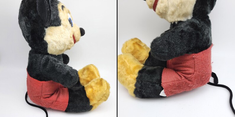 May include: Vintage Mickey Mouse plush toy. The plush features a black body, red shorts, yellow feet, and a cream-colored face. The toy has a black tail and is in a seated position.