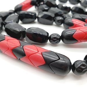 May include: A black and red beaded necklace with alternating geometric shapes. The beads are made of a smooth, glossy material.