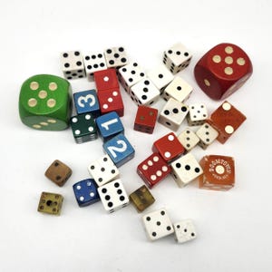 May include: A collection of various dice in different colors and sizes. Includes red, green, white, blue, and brown dice. Some dice have numbers, while others have dots. One die has the text "BOOMTOWN VERDI NEV".
