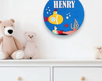 May include: A blue and yellow wooden sign with the name "HENRY" in white letters. The sign features a yellow submarine with red accents, a red crab, and coral.