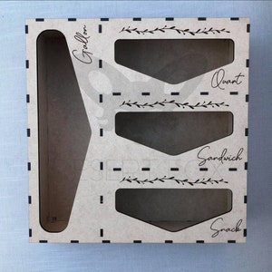 May include: A light brown wooden storage organizer with compartments labeled "Gallon", "Quart", "Sandwich", and "Snack". The organizer has a decorative floral design and is designed to hold various sized bags.