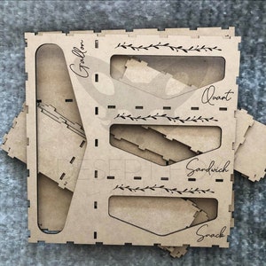 May include: A laser-cut wooden organizer with compartments labeled "Gallon", "Quart", "Sandwich", and "Snack". The organizer has a natural wood finish and includes decorative floral accents. Includes several separate pieces.