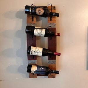 May include: A wooden wine rack with four bottles of wine. The rack is made from reclaimed wood and has a rustic look. The bottles are all different colours and have different labels.