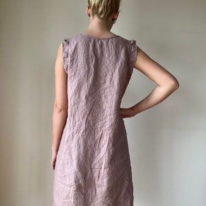 May include: A mauve linen dress with a ruffled neckline and sleeves. The dress has a relaxed fit and a slightly A-line silhouette.