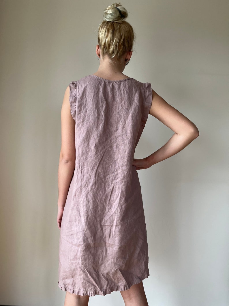May include: A mauve linen dress with a ruffled neckline and sleeves. The dress has a relaxed fit and a slightly A-line silhouette.