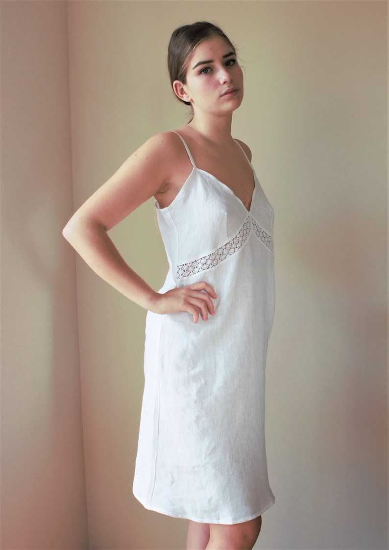 May include: A white linen slip dress with a lace trim around the neckline. The dress has a simple, classic design and is perfect for a casual or formal occasion.