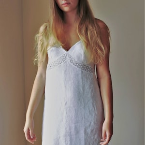 May include: A white linen slip dress with a lace trim around the neckline. The dress has a simple, elegant design and is perfect for a summer evening.
