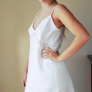 May include: A white linen slip dress with a lace trim around the neckline. The dress has a simple, classic design and is perfect for a casual or formal occasion.