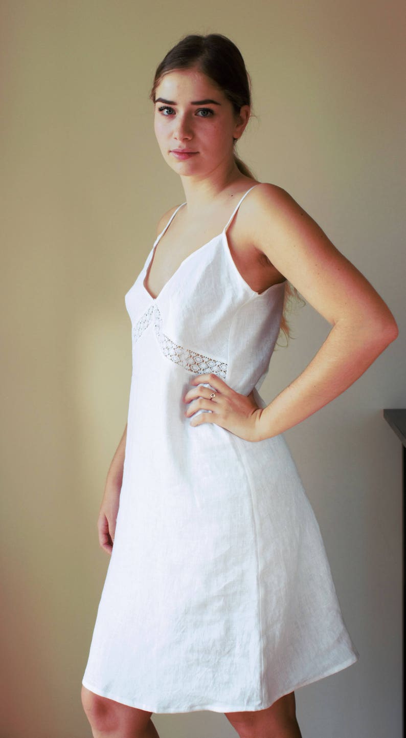 May include: A white linen slip dress with a lace trim around the neckline. The dress has a simple, classic design and is perfect for a casual or formal occasion.