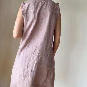May include: A sleeveless, light pink linen dress with a ruffled neckline and ruffled straps. The dress is made of a soft, lightweight fabric and has a relaxed fit.