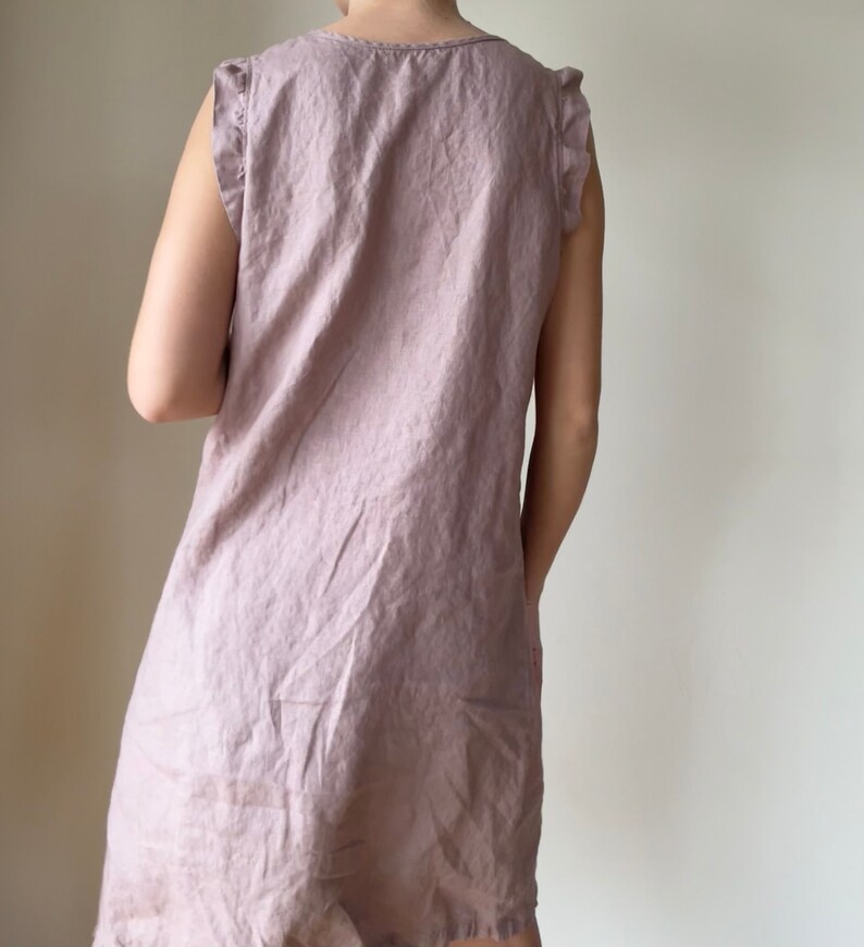 May include: A sleeveless, light pink linen dress with a ruffled neckline and ruffled straps. The dress is made of a soft, lightweight fabric and has a relaxed fit.