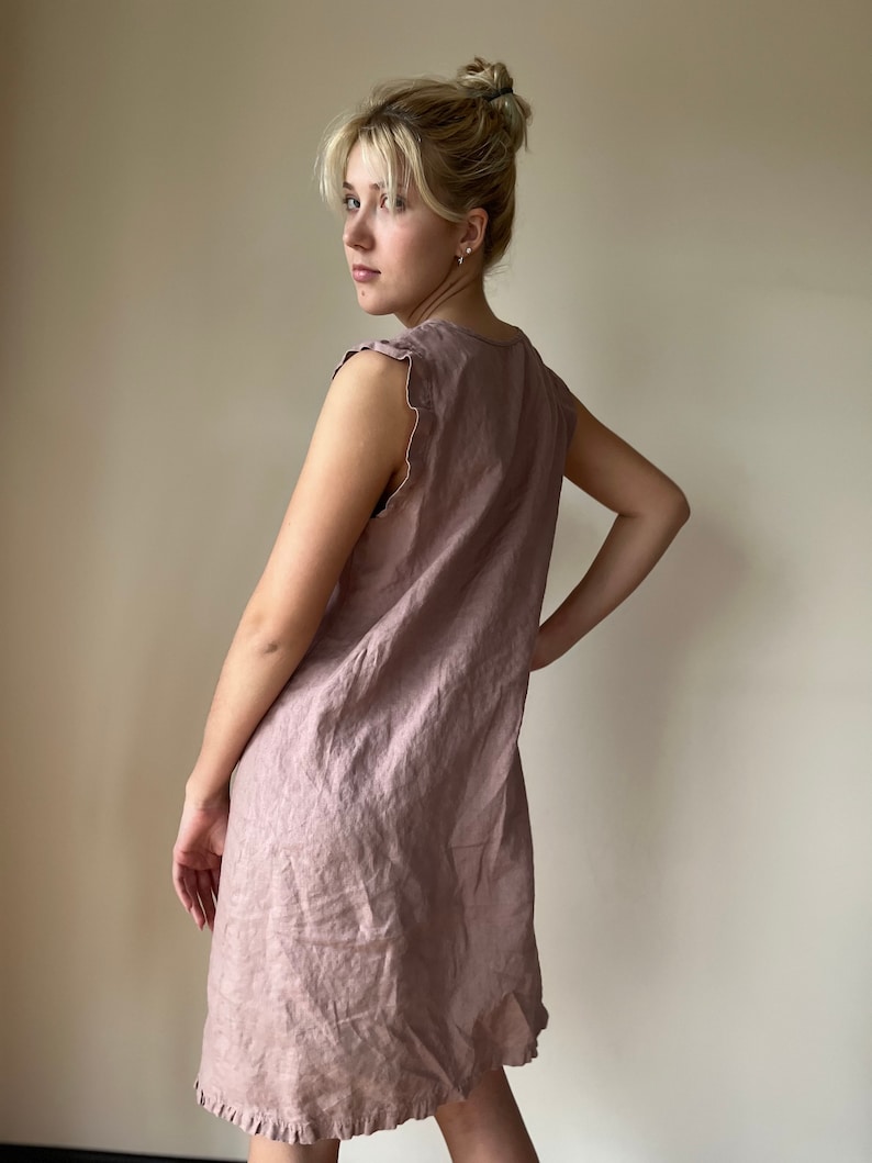May include: A mauve linen dress with a ruffled hem and sleeveless design.