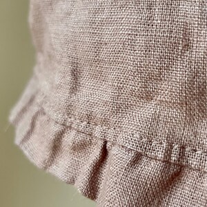 May include: A close-up of a light brown linen fabric with a ruffled edge. The fabric has a woven texture and a subtle sheen.