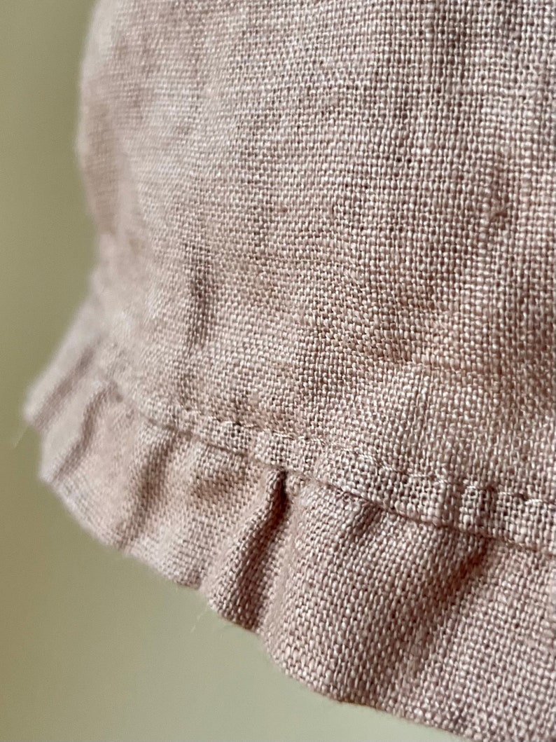 May include: A close-up of a light brown linen fabric with a ruffled edge. The fabric has a woven texture and a subtle sheen.