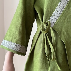 May include: A green linen wrap top with a white lace trim. The top has a tie closure at the waist.
