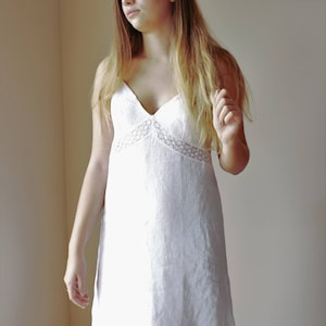 May include: A white linen slip dress with delicate lace trim around the neckline. The dress has a v-neck and a relaxed fit.