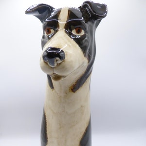 May include: A ceramic dog sculpture with black and white markings. The dog has a long snout and large, expressive eyes. The sculpture is glazed in a brown and white finish.