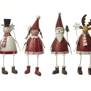 Puede incluir: Cuatro figuras navide&ntilde;as caprichosas. Un mu&ntilde;eco de nieve, una ni&ntilde;a, Pap&aacute; Noel y un reno, cada uno con piernas colgantes y vistiendo atuendos festivos. El mu&ntilde;eco de nieve tiene un sombrero de copa y una bufanda. Pintado en rojo, blanco y marr&oacute;n.