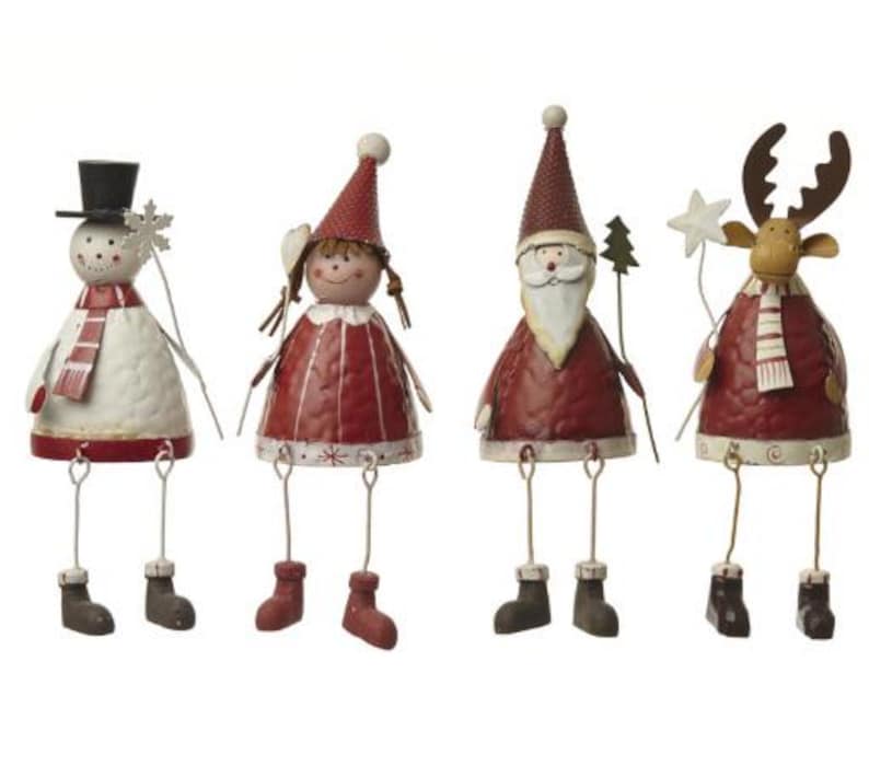 Puede incluir: Cuatro figuras navide&ntilde;as caprichosas. Un mu&ntilde;eco de nieve, una ni&ntilde;a, Pap&aacute; Noel y un reno, cada uno con piernas colgantes y vistiendo atuendos festivos. El mu&ntilde;eco de nieve tiene un sombrero de copa y una bufanda. Pintado en rojo, blanco y marr&oacute;n.