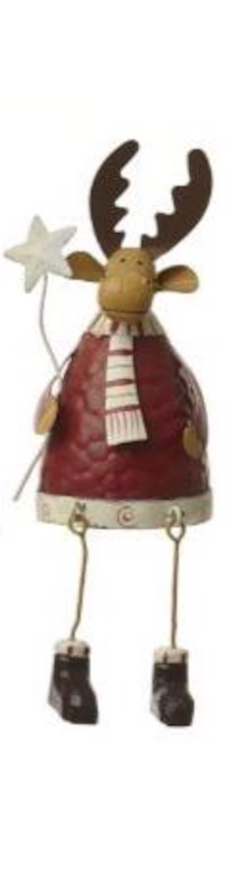 Puede incluir: Adorno navide&ntilde;o de metal con forma de alce. El alce tiene cuernos marrones, un cuerpo rojo y una bufanda a rayas. Sostiene una varita de estrella y lleva botas marrones. El adorno tiene un dise&ntilde;o vintage y r&uacute;stico.