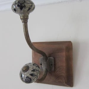 May include: A single wooden wall hook with a ceramic knob. The knob is white with black floral designs. The hook is mounted on a square wooden base.