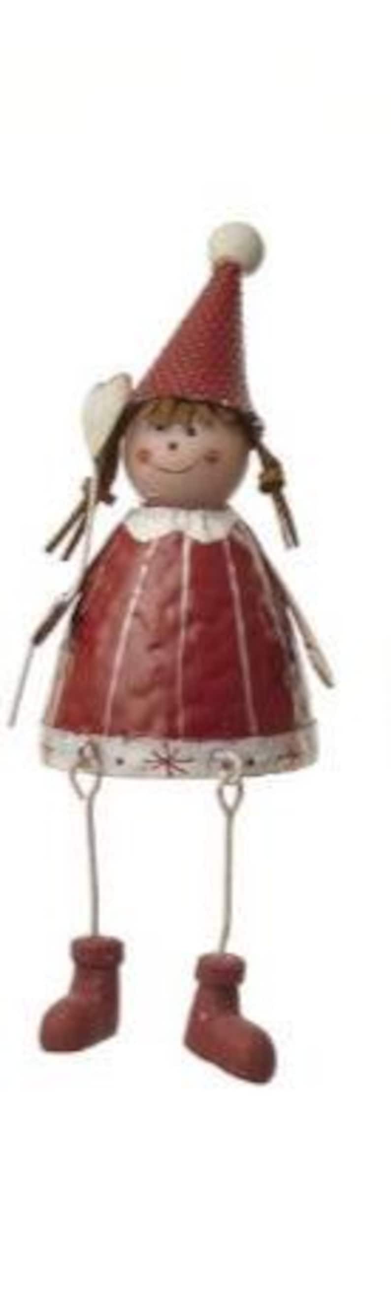Puede incluir: Figura decorativa de metal de una ni&ntilde;a. Lleva un gorro c&oacute;nico rojo con un pomp&oacute;n blanco y un vestido rojo a juego. La figura tiene piernas, brazos y botas marrones de alambre. La cara est&aacute; pintada con una expresi&oacute;n sonriente. Un adorno encantador.