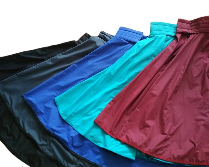 May include: A collection of colorful, water-resistant skirts in various shades, including black, navy, blue, teal, and burgundy. Each skirt features a structured waistband and a flowing, A-line silhouette, ideal for outdoor activities or travel.
