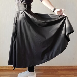 May include: A black, flowing skirt with a wide waistband and a buckle closure. The skirt is made of a lightweight fabric that drapes elegantly. The skirt is shown in a full-length view, with the hemline reaching the ankles.