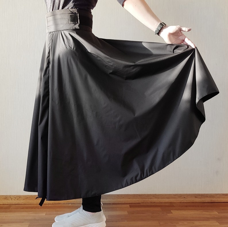 May include: A black, flowing skirt with a wide waistband and a buckle closure. The skirt is made of a lightweight fabric that drapes elegantly. The skirt is shown in a full-length view, with the hemline reaching the ankles.