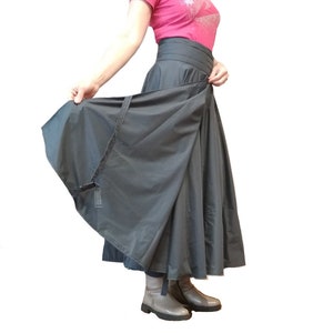 May include: A dark gray wrap skirt with a wide waistband and a flowing, full length. The skirt is being held open to display its shape and construction. The fabric appears to be a lightweight material.